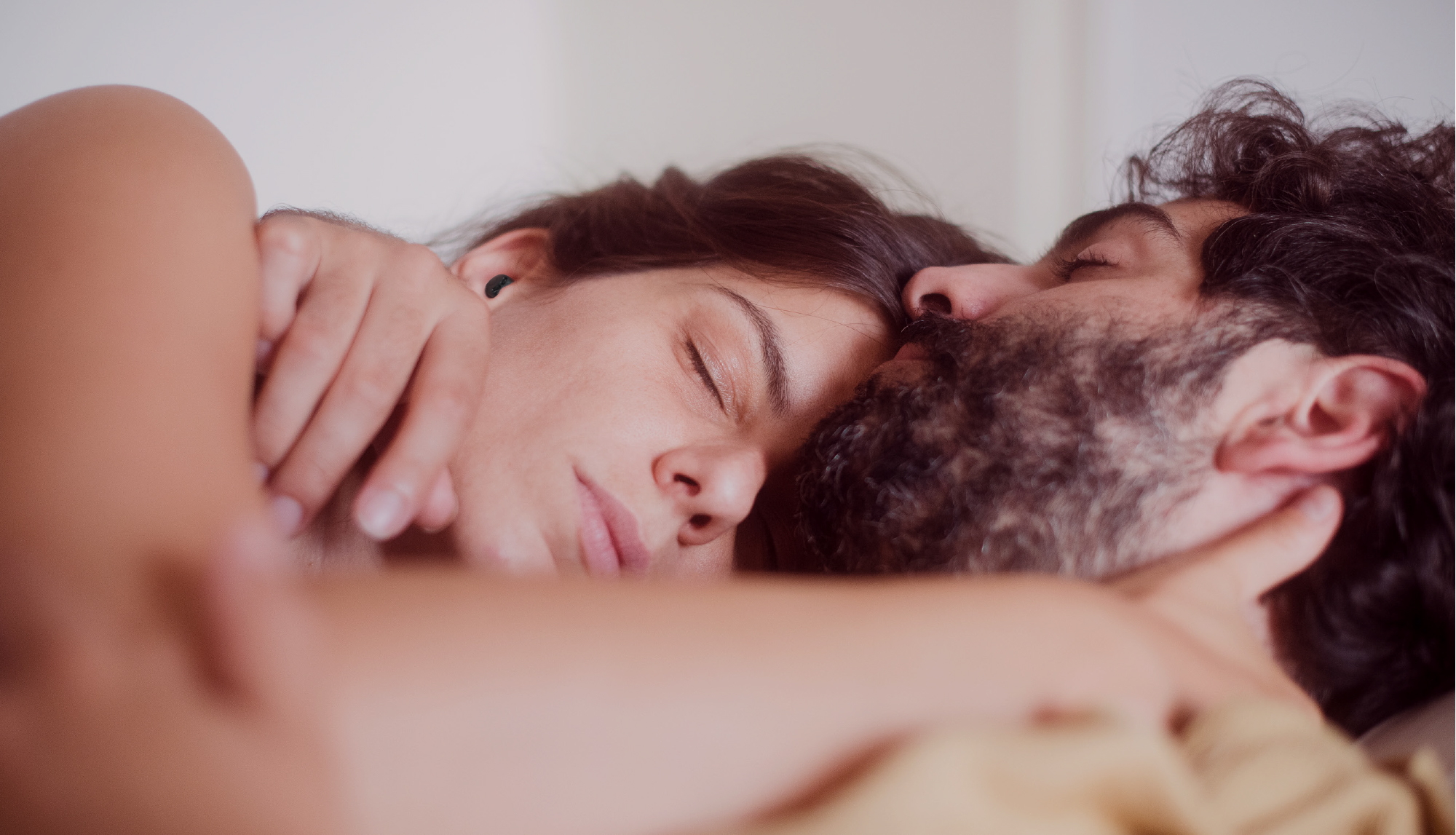 Woman sleeping peacefully with QuietOn 4 active noise-canceling earbuds while partner snores beside her in bed.