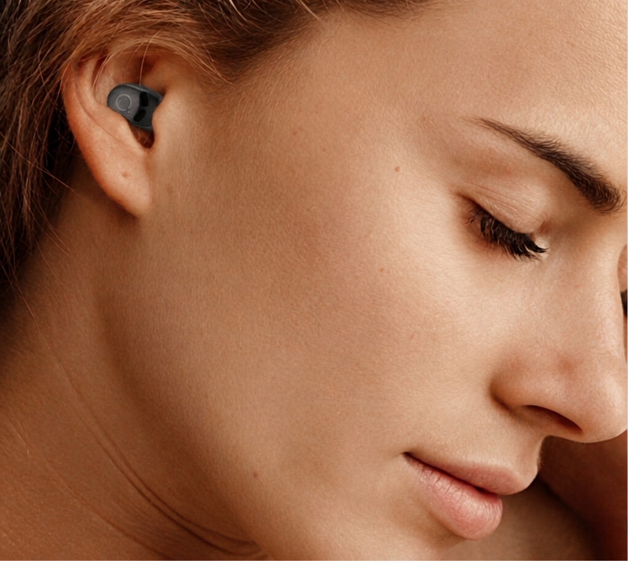 Woman wearing QuietOn 4 sleep earbud close-up showing slim low-profile fit in ear — comfortable noise cancelling earbud designed for side sleepers