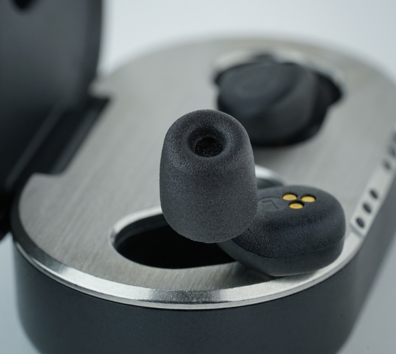 QuietOn 4 sleep earbud sitting in open charging case showing memory foam ear tip and gold charging contacts — compact ANC sleep earbud with wireless charging case