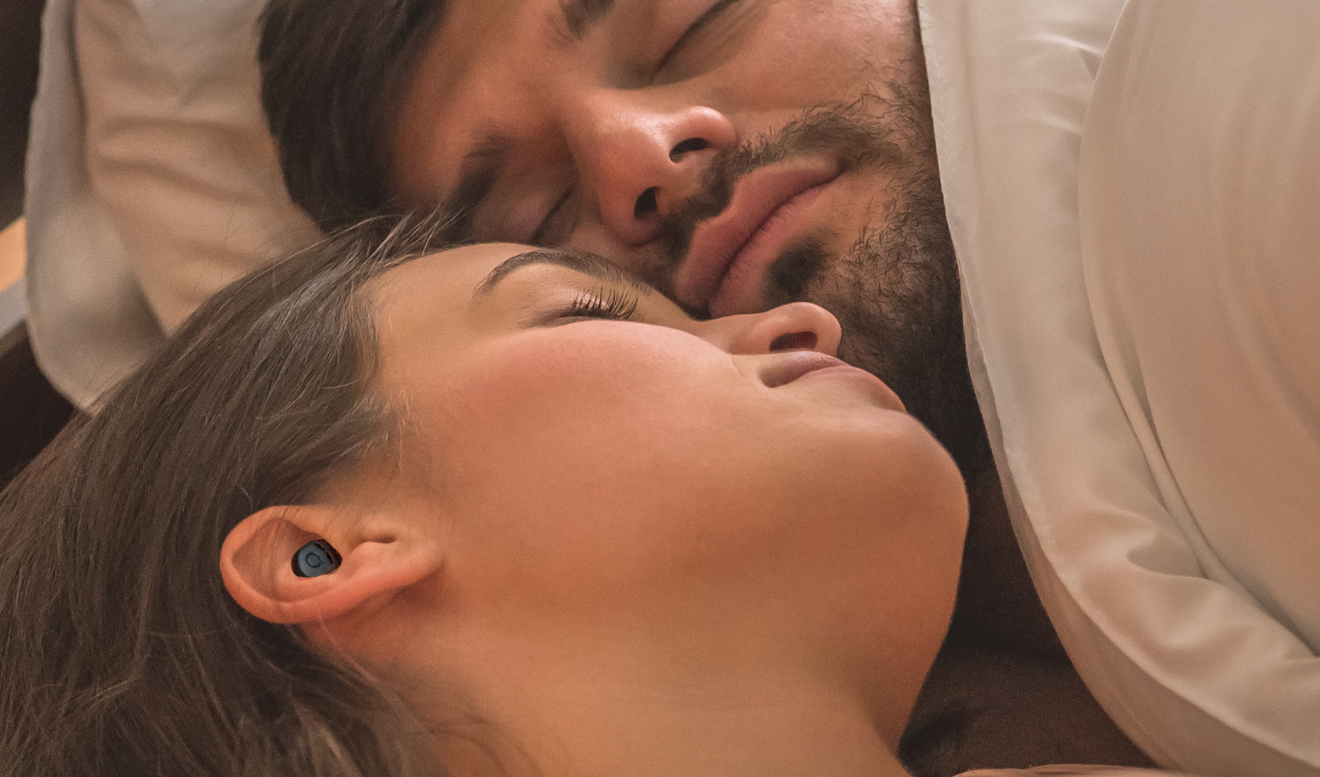Woman sleeping next to snoring partner wearing QuietOn 4 sleep earbud — noise cancelling earbuds for blocking snoring and sleeping peacefully beside a partner